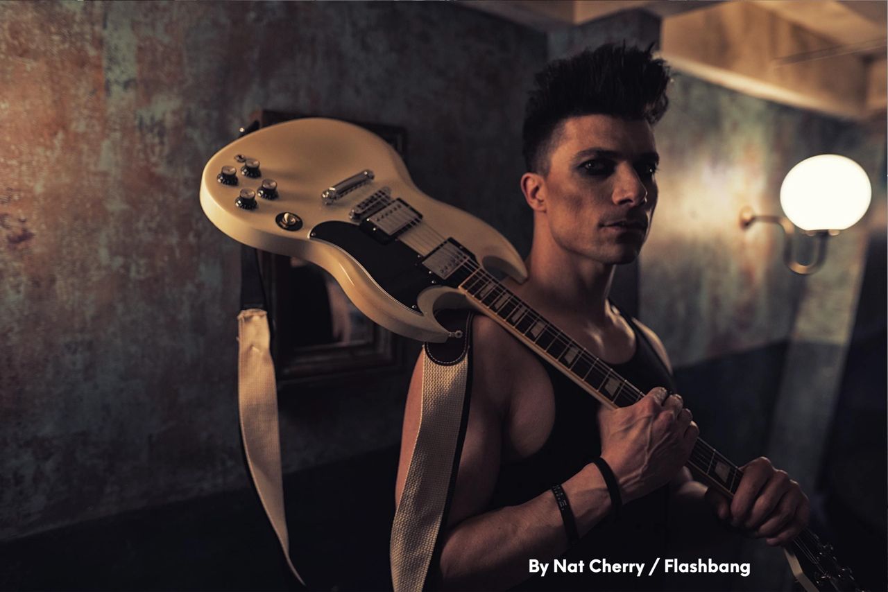 Ben Christo — press portrait, holding a white SG-style guitar, by Nat Cherry / Flashbang