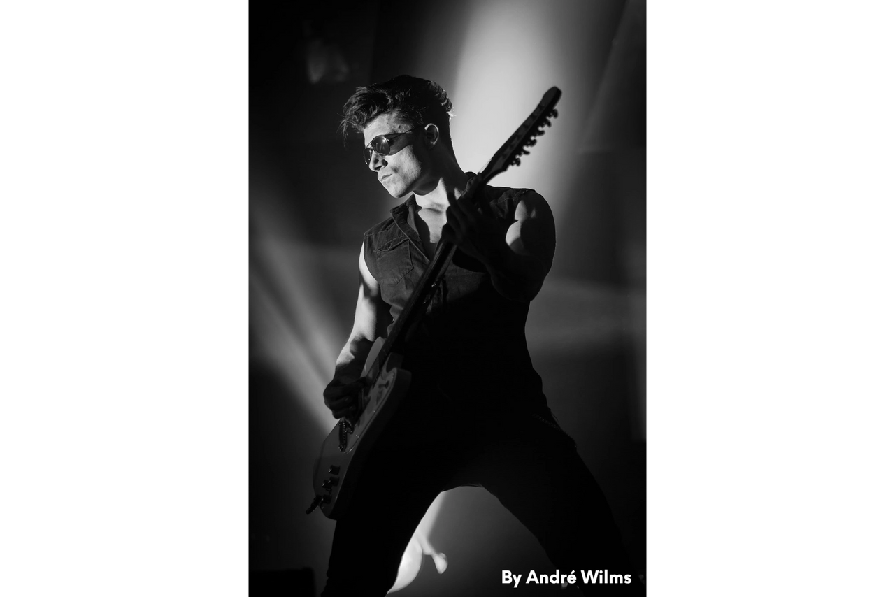 Ben Christo playing guitar on stage, soft spotlight from above — black and white