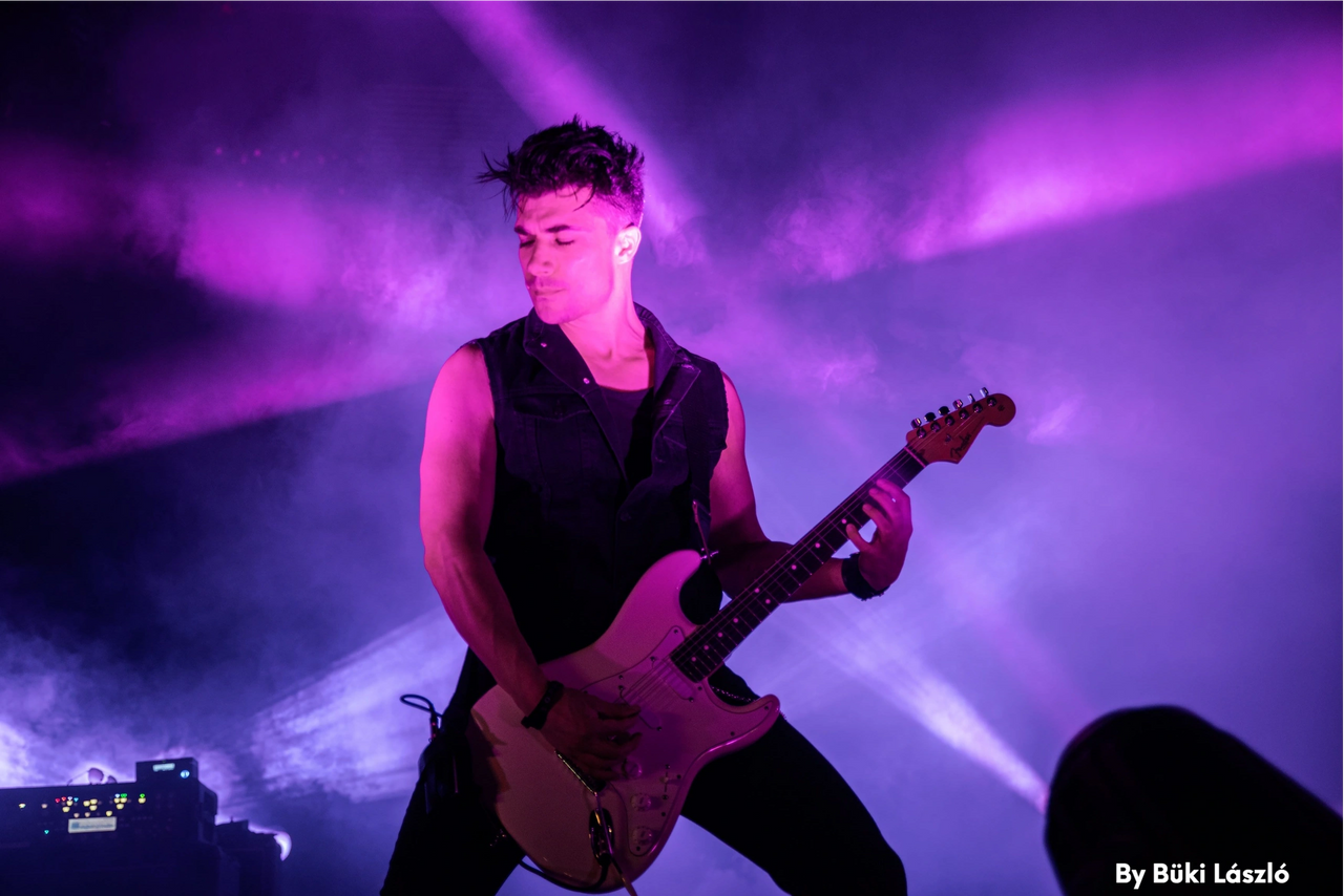 Ben Christo performing on stage in vivid purple and magenta stage lighting