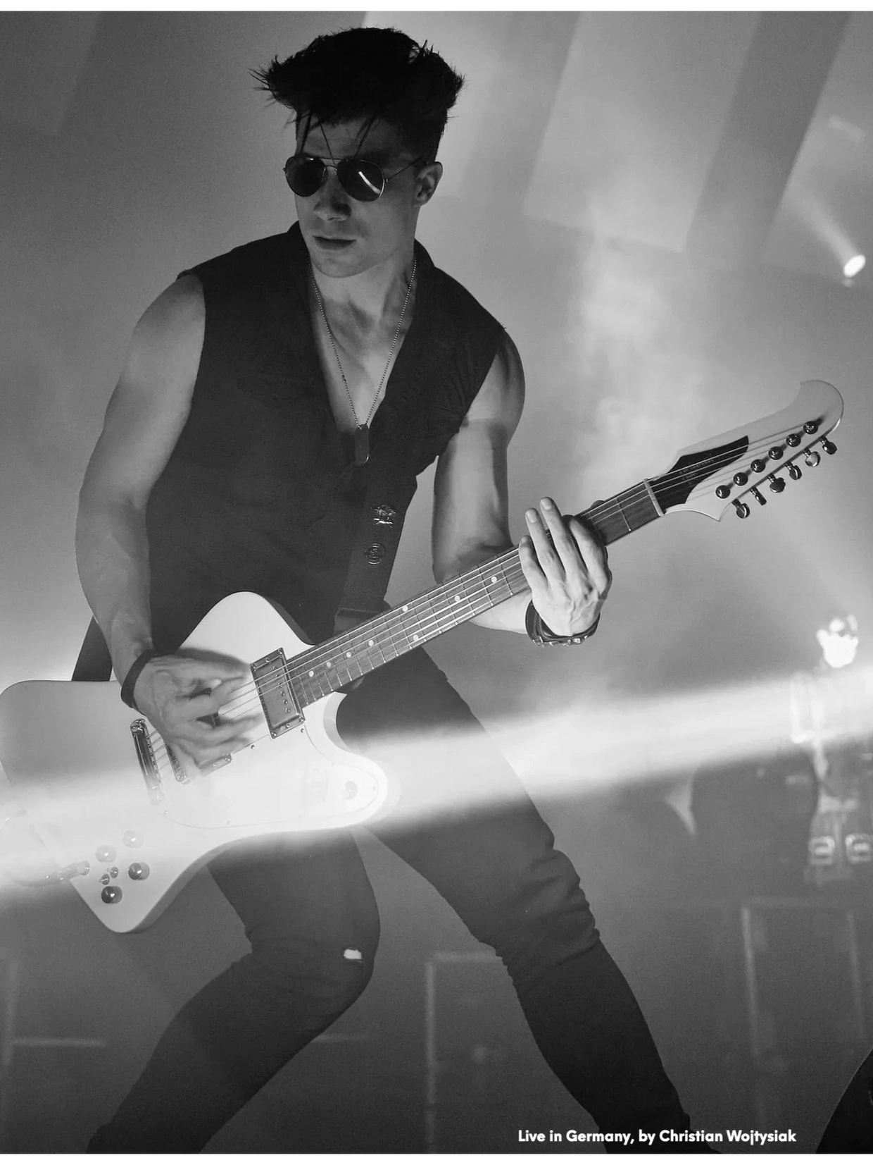 Ben Christo playing white guitar on stage in Germany — black and white, light beams crossing frame