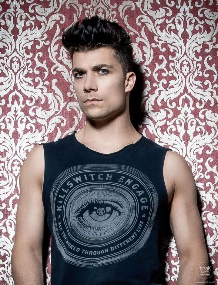 Ben Christo — editorial portrait against red damask wallpaper, wearing Killswitch Engage vest